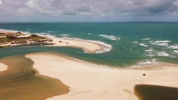 Vista aérea panorámica de la playa con un pequeño pueblo y gente divirtiéndose en la arena. video