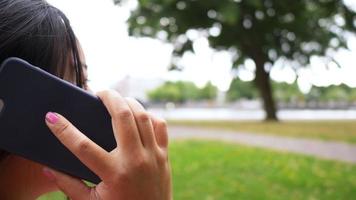 close-up achteraanzicht van aisan vrouw zitten en bellen op smartphone in het park. uitrusten met goed uitzicht. uitgaan in het weekend. gaan picknicken concept video