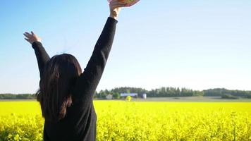 Back view of happy young woman standing and raising hands up then taking hat off and throwing it on the sky at Beautiful Field with Yellow Flowers , enjoying Nice Nature
