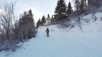 un enfant grimpe sur une route enneigée avec des peaux de phoque sur des skis de randonnée