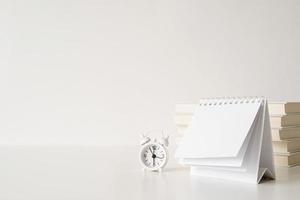 Mock up blank spiral calendar with flipping sheets on white table with stack of books, glasses and clock photo