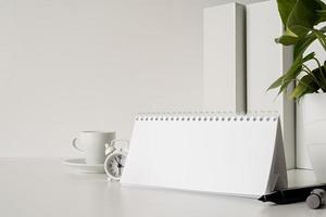 Mock up blank spiral calendar with flipping sheets on white table with coffee, stationery and clock photo