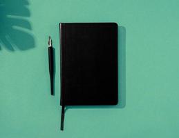 Minimal style black notebook and pens top view on green background, palm tree shadow overlay photo