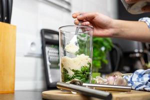 la persona que agrega el queso rallado al recipiente de licuado. preparación de pesto. foto