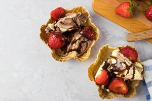 Ice cream dessert in a waffle with strawberries on a white table from above photo