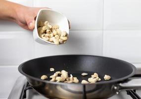 A person throwing cashews into the pan. Roasted nuts.
