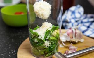 la persona que agrega el queso rallado al recipiente de licuado. preparación de pesto. foto