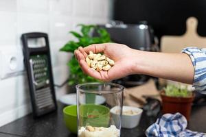 la persona que pone anacardos en el recipiente de licuado. preparación de pesto de albahaca italiana. foto