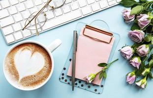 Workspace with keyboard, clipboard, roses on pastel blue background. photo