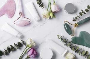 productos cosméticos, tubos de crema, rodillo facial y eucalipto sobre fondo de mármol. foto