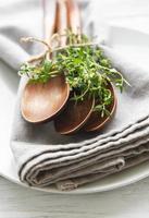 Wooden spoons on a plate and linen napkins decorated with green bunches of thyme