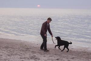 Joven caminando por la playa por la mañana con perro negro