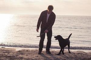 young man walking  on the morning beach with black dog photo