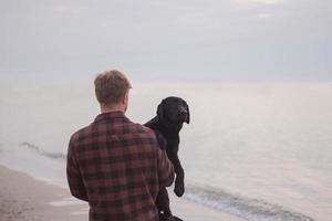 young man walking  on the morning beach with black dog photo