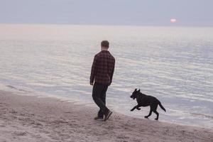 Joven caminando por la playa por la mañana con perro negro