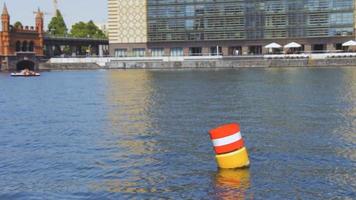 Boya flotante de navegación de acero rojo y blanco amarillo en el agua del río Spree azul
