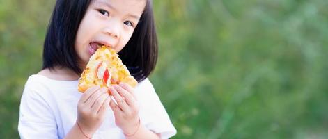 Child's hand holds delicious pizza. Kid girl are happy to eat food. Empty space to enter text. photo