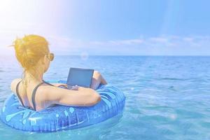Girl is resting on sea on inflatable ring with mini-computer. photo