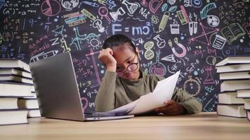 serieus klein Aziatisch meisje dat huiswerk controleert en online studeert op laptop in werkkamer thuis. laptop op tafel zetten en papier zoeken. online concept studeren