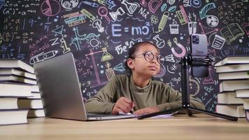 Tired Asian girl wearing glasses thinking and getting idea and taking note when looking at smartphone at home. Setting laptop and smartphone on the table and Studying online concept video