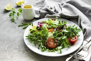 Fresh green mixed  salad bowl with tomatoes and microgreens  on  concrete background. Healthy food, top view. photo