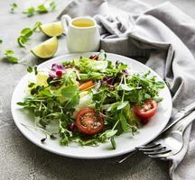 Fresh green mixed  salad bowl with tomatoes and microgreens  on  concrete background. Healthy food, top view. photo