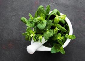 Fresh mint leaves in mortar on stone table. Top view photo