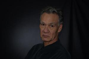 Dramatic Portrait of a Mature Man against a Black Background wearing a Black Shirt photo