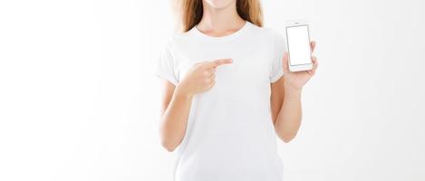 young girl, woman in t-shirt pointing finger at blank screen mobile phone isolated on white background. Hand holding smartphone. Copy space photo