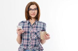 Beautiful woman with glasses holding mug smartphone. Young lady drinking tea and using gadget. Break concept. Isolated side view on white background.