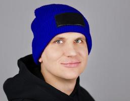 hipster in a blue hat and a hoodie with a hood on a gray background photo