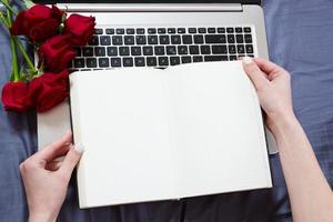Close up - Hands holding an open notebook top view mock up. Topview on laptop keyboard and bouquet of flowers background photo