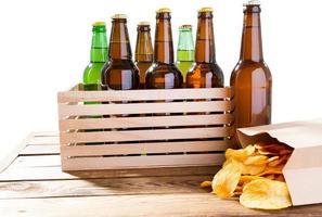 Photo of different full beer bottles with no labels and paper pack of potato chips on table