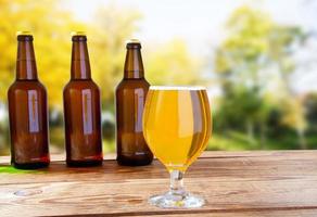 cup of cider,beer and bottles on wooden table on blurred park background photo