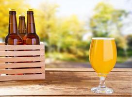 cup of beer and bottles on wooden box on table on blurred park background photo