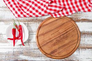 Vista superior mantel rojo arrugado, pimiento picante y plancha sobre mesa de madera, maqueta