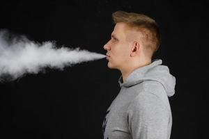 hombres en sudadera con capucha vapean y liberan una nube de vapor. enfoque selectivo foto