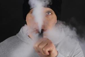 Unrecognizable man in the cloud of vape smoke. Guy smoking e-cigarette to quit tobacco. Vapor and alternative nicotine free smoking concept, copy space selective focus photo