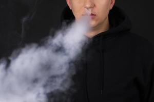 Unrecognizable man in the cloud of vape smoke. Guy smoking e-cigarette to quit tobacco. Vapor and alternative nicotine free smoking concept, copy space selective focus photo