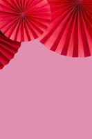 Red paper fans on a pink background copy space. Vertical format photo