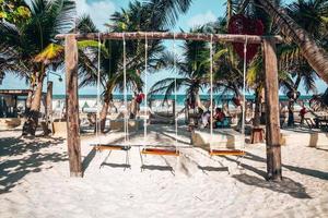 Empty swing and heart shape artwork hanging on tree at beach resort with tourists spending leisure time photo