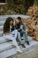 pareja joven sentada en las escaleras al aire libre en un día de otoño y usando un teléfono móvil foto