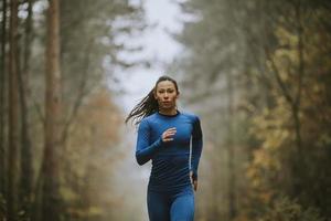 Mujer joven corriendo hacia la cámara en la pista forestal en otoño foto