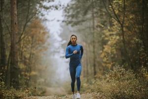 Young woman running toward camera on the forest trail at autumn photo