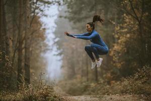 Young woman taking high jump on the forest trail at autumn