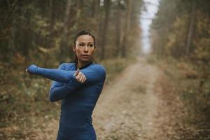 Mujer joven en traje de pista azul que se extiende antes de entrenar en el bosque de otoño