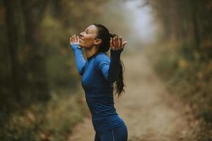 Mujer joven en traje azul abriendo los brazos y respirando profundamente en un bosque foto