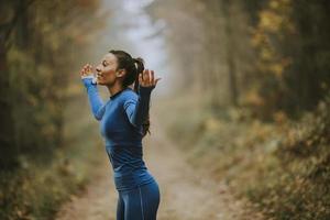 Young woman in blue track suit spreading arms and taking deep breath in a forest
