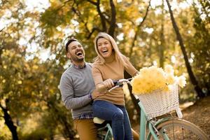 Pareja joven activa disfrutando de andar en bicicleta en el parque otoño dorado foto