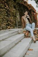 Mujer joven bebiendo café para llevar en las escaleras exteriores en día de otoño foto